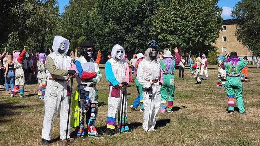 People dressed up with colourful wigs, masks and overalls, standing on a grass field.